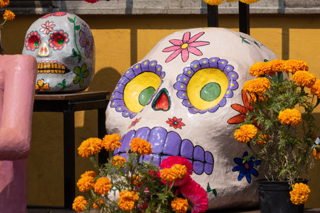 A large, painted skull is placed on a table next to a vase filled with orange flowers. Mexican Day of the Dead tradition, offerings, food, colors, decorations, and papel picado, La Catrina.の写真素材