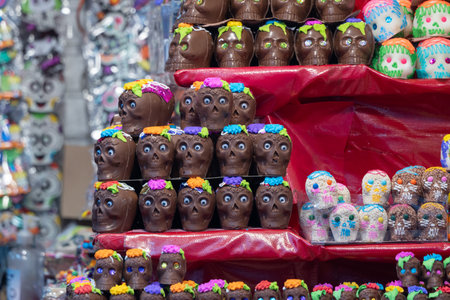 A display of chocolate skulls with flowers on them. The skulls are arranged in a pyramid shape. Mexican Day of the Dead tradition, offerings, food, colors, decorations, and papel picado, La Catrina.の写真素材