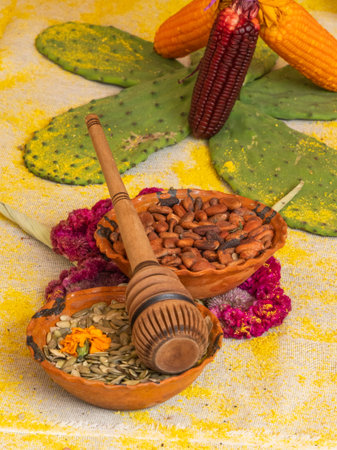 A wooden spoon rests on a table, next to a bowl filled with nuts and seeds. Mexican Day of the Dead tradition, offerings, food, colors, decorations, and papel picado.の写真素材