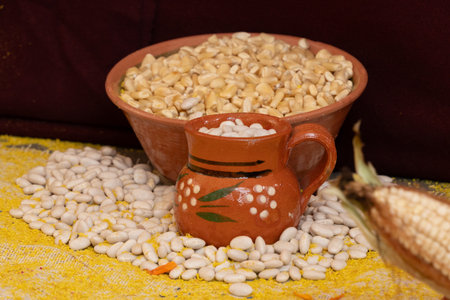 A bowl of white beans and a small, decorative ceramic pot with a leaf design on it. Mexican Day of the Dead tradition, offerings, food, colors, decorations, and papel picado.の写真素材