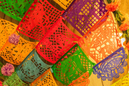 A colorful array of paper lanterns with pom poms hanging from them. The colors are bright. Mexican Day of the Dead tradition, offerings, food, colors, decorations, and papel picado.の写真素材
