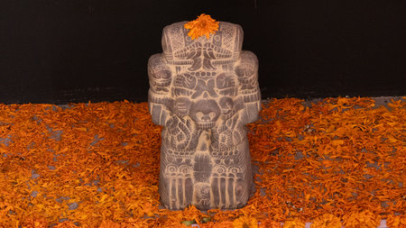 A statue of a man with a red flower on his head. The statue is surrounded by orange leaves. Mexican Day of the Dead tradition, offerings, food, colors, decorations, and papel picado, La Catrina.の写真素材