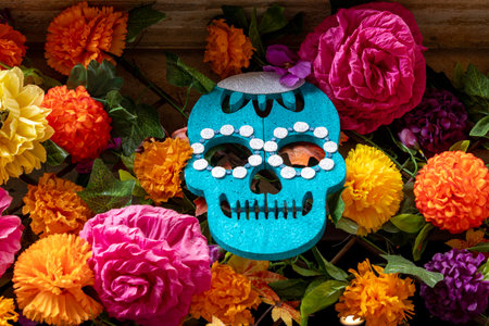 A blue skull is surrounded by a colorful bouquet of flowers. The skull is decorated with white beads. Mexican Day of the Dead tradition, offerings, food, colors, decorations, and papel picado, La Catrina.の写真素材