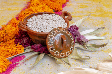A bowl of beans is sitting on a table with flowers. The bowl is decorated with a lid. Mexican Day of the Dead tradition, offerings, food, colors, decorations, and papel picado, La Catrina.の写真素材
