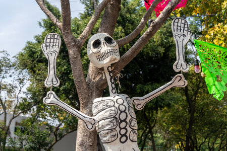 A skeleton is holding up its arms and legs, with a green and pink decoration on the tree behind it. Mexican Day of the Dead tradition, offerings, food, colors, decorations, and papel picado, La Catrina.の写真素材