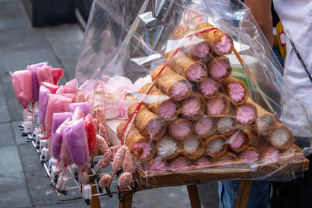 A vendor is selling a variety of pink pastries in plastic bags, with a person standing behind the ta. Mexican Day of the Dead tradition, offerings, food, colors, decorations, and papel picado.の写真素材