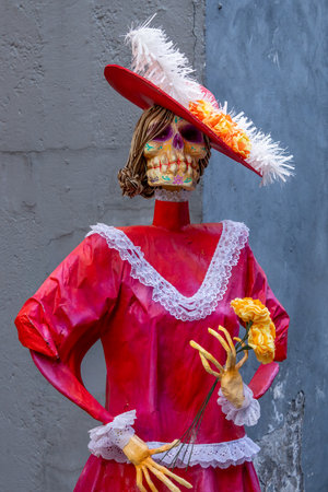 A woman in a red dress with a flower in her hand. The woman is dressed in a skeleton costume. Mexican Day of the Dead tradition, offerings, food, colors, decorations, and papel picado, La Catrina.の写真素材