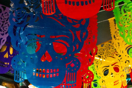A colorful display of paper skulls hanging from the ceiling. The skulls are of different colors. Mexican Day of the Dead tradition, offerings, food, colors, decorations, and papel picado, La Catrina.の写真素材
