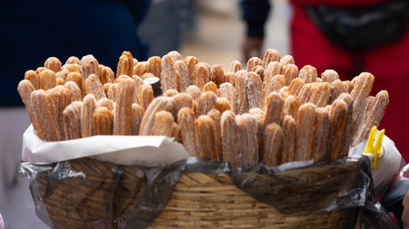 A basket of churros is displayed on a table. The churros are covered in sugar. The scene is inviting. Mexican Day of the Dead tradition, offerings, food, colors, decorations, and papel picado, La Catrina.の写真素材