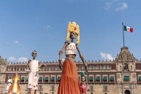 A skeleton dressed in a yellow hat stands in front of a building. The skeleton is holding a red. Mexican Day of the Dead tradition, offerings, food, colors, decorations, and papel picado.の写真素材