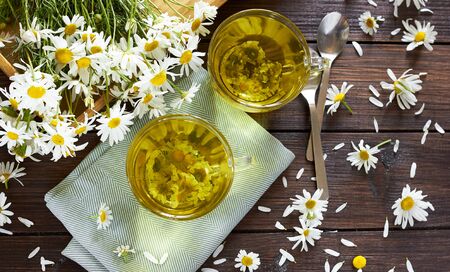 Chamomile herbal tea with flower buds nearby on wooden table with textile and camomile bouquet, closeup, copy space, healthy herbal drinks and natural healer conceptの写真素材