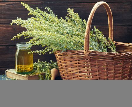 Absinth blooming herb in a wicker on wooden rustic background with bunch of sagebrush flowers, mortar and blossoms all around on old books, closeup, copy space, alternative medicine conceptの写真素材