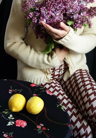 Woman holding a bouquet of blooming lilac sitting at the table with lemons on it, body part crop, closeup, copy space, verticalの写真素材