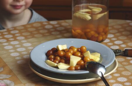 Child at the kitchen  table with stewed fruit compote- zucchini and cherry plum on the plate, crop,...