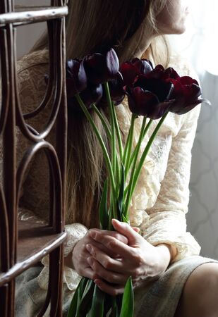 Young bohemian woman in vintage retro cloth and a hat smelling bouquet of purple tulips, creative sensual female portrait, verticalの写真素材