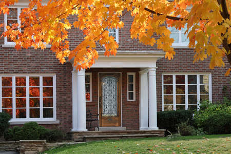 front door of traditional two story brick house with maple tree in brilliant fall colorの写真素材