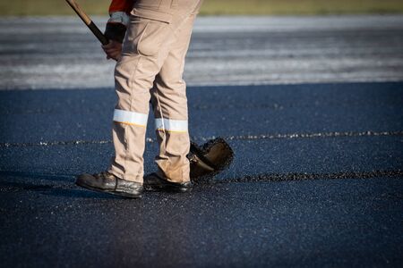 Worker with roller compacting asphalt on a road