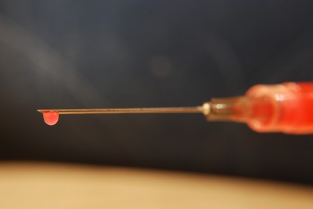 Close-up of a needle and syringe with a drop of thinned blood.の写真素材
