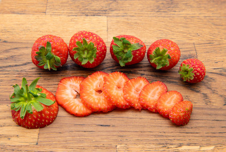 Strawberries on a wooden chopping board with one sliced into segmemts.の写真素材