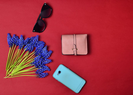 Women's accessories are lined on a red background. Smartphone, purse, sunglasses, wild flowers. Flat lay. Top view.の写真素材