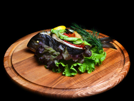 Baked fish with vegetables on a wooden board.の写真素材