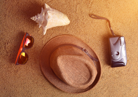 Beach accessories lie on the sand.Hat, camera, sunglasses, shell. The concept of relaxing at sea. Summer beach season is open! Top view.の写真素材