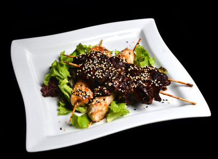 Yakitori with sesame seeds on a plate. Fried chicken meat and chicken liver on sticks close-up isolated on a black background. Top view.の写真素材