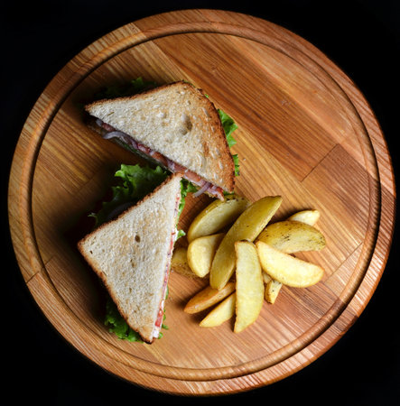 Sandwich with fried potatoes on a wooden board isolated on a black background. Top view. Restaurated food. Fast food.の写真素材