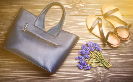 Women's accessories on the wooden floor. Sandals, women's bag, a bouquet of dove flowers. Top view. Flat lay.の写真素材