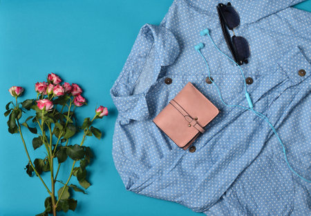 Women's clothing and accessories laid out on a blue background. Shirt, purse, sunglasses, headphones, bouquet of roses. Top View. Flat lay.の写真素材
