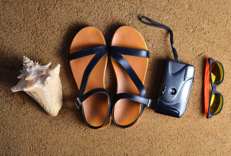 Beach accessories lie on the sand.Camera, sandals, sunglasses, seashells. The concept of relaxing at sea. Summer beach season is open! Top view.の写真素材