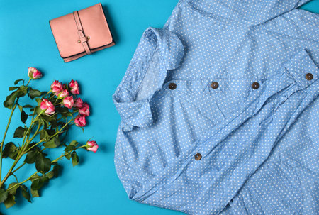 Women's clothing and accessories laid out on a blue background. Shirt, purse, bouquet of roses. Top View. Flat lay.の写真素材
