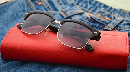 Women's things and accessories. Classic sunglasses, red leather purse, jeans.