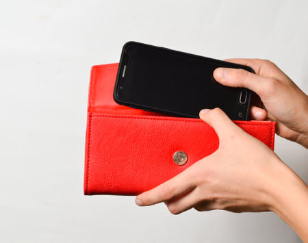 Female hands lay smartphone in red leather purse isolated on white background.の写真素材