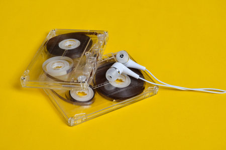 Retro technology. Plastic transparent audio cassette and white vacuum headphones on a bright yellow...