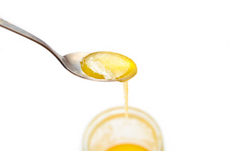 A metal spoon with bee honey close-up isolated on white background.