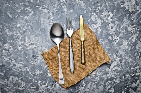 Antique spoon, fork, knife on a napkin lie on a gray concrete table. Top view.