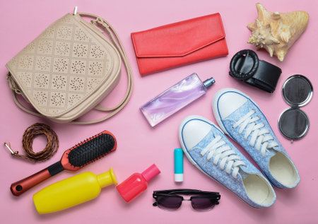 What's in the women's bag? Going on a trip. Girly fashionable spring and summer accessories: sneakers, cosmetics, beauty and hygiene products, a bag, sunglasses on a pink pastel background. Top view.の写真素材