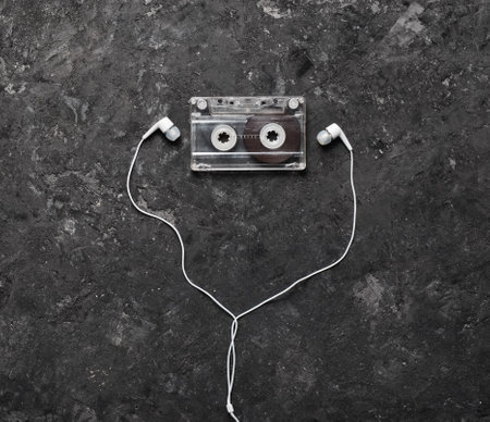 Conceptual photo illustrating the love of music. Audio cassette and headphones on a black concrete background. Top view.の写真素材