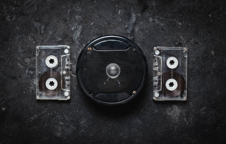 Acoustic speaker and audio cassette on a black concrete table. Retro technology. Meloman. Top view....