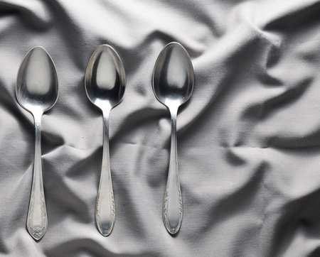 A set of three metal spoons on a gray silk tablecloth. Top view.の写真素材