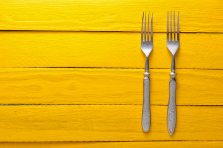 Two antique forks on a wooden table in yellow. Top view. Copy space.