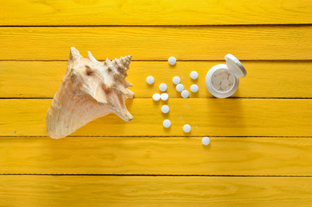 Minerals for health and beauty. Tablets of calcium, shell on a yellow wooden table. Top view....