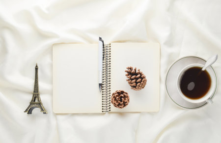 Morning inspiration, cup of tea, notebook with a pen, pine cone, souvenir on a white bed sheet....