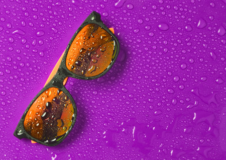 Fashion sunglasses in drops of water on a bright violet background. Top view.の写真素材
