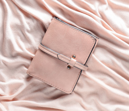 Female leather purse on a pink fabric background. Top view.
