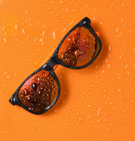 Fashion sunglasses in drops of water on a bright orange background. Top view.の写真素材