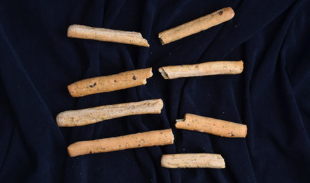 Broken bread sticks on a black fabric background. Top view.
