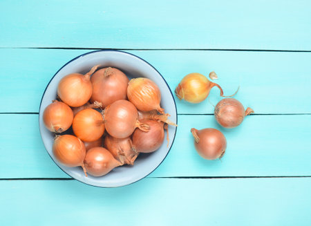 Many onions in a bowl on a turquoise-colored wooden table. Vegetable concept.の写真素材