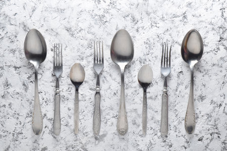 A set of grunge metal spoons and forks on a white concrete surface. Top view.